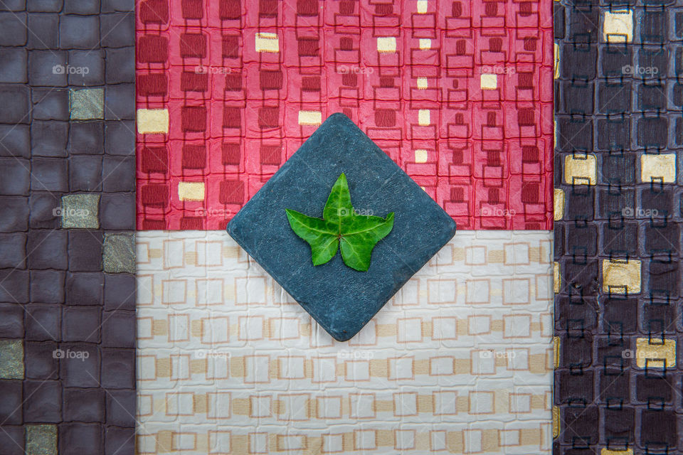 Flat lay of square textured backgrounds different colors and a square shaped stone with a single ivy leaf as contrast