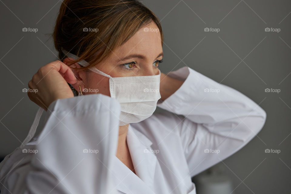 Doctor with face covered with mask. Portrait of young woman wearing the uniform, cap and mask to avoid virus infection and to prevent the spread of disease. Real people, authentic situations