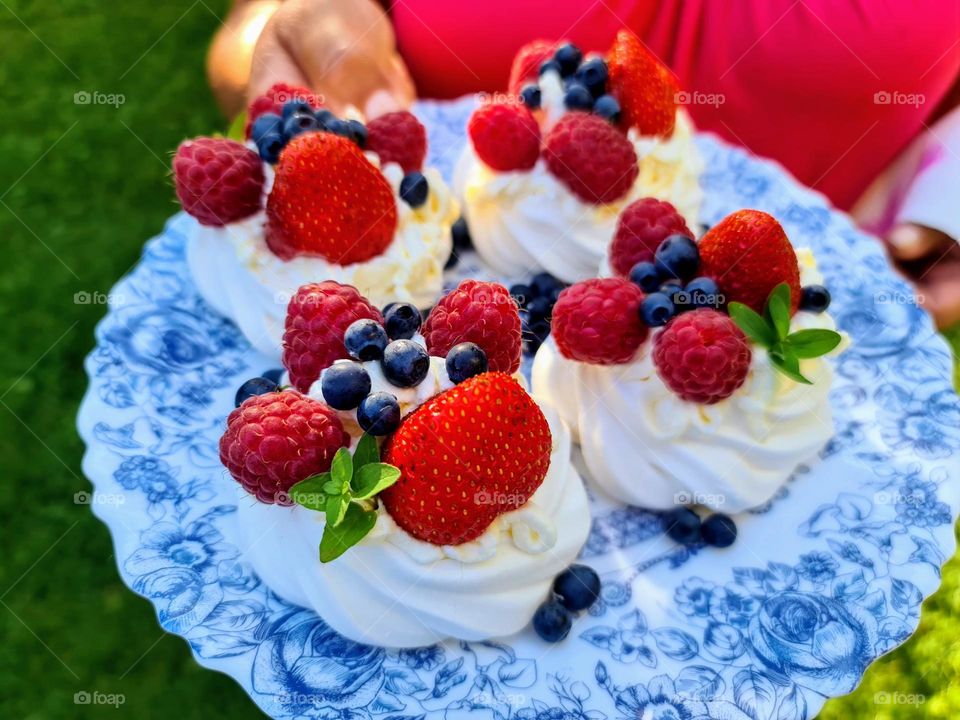 Delicious sweet meringue dessert with fresh berries strawberries, blueberries and raspberries on the blue and white plate held by a woman in the bright fuchsia top