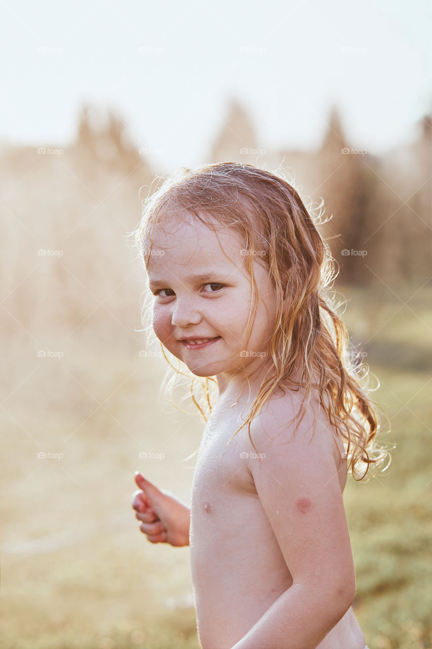 Little cute adorable girl enjoying a cool water sprayed by her mother during hot summer day in backyard. Candid people, real moments, authentic situations