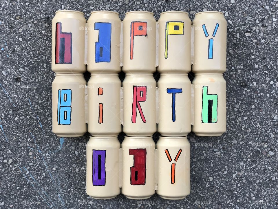 Happy Birthday message with colored beer cans over asphalted road