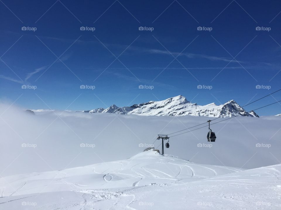 A view of ski lift cabin against blue sky. High in the mountains covered in snow. Italy