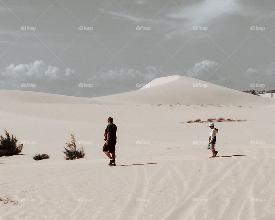 A man and a boy are walking on a sand dunes