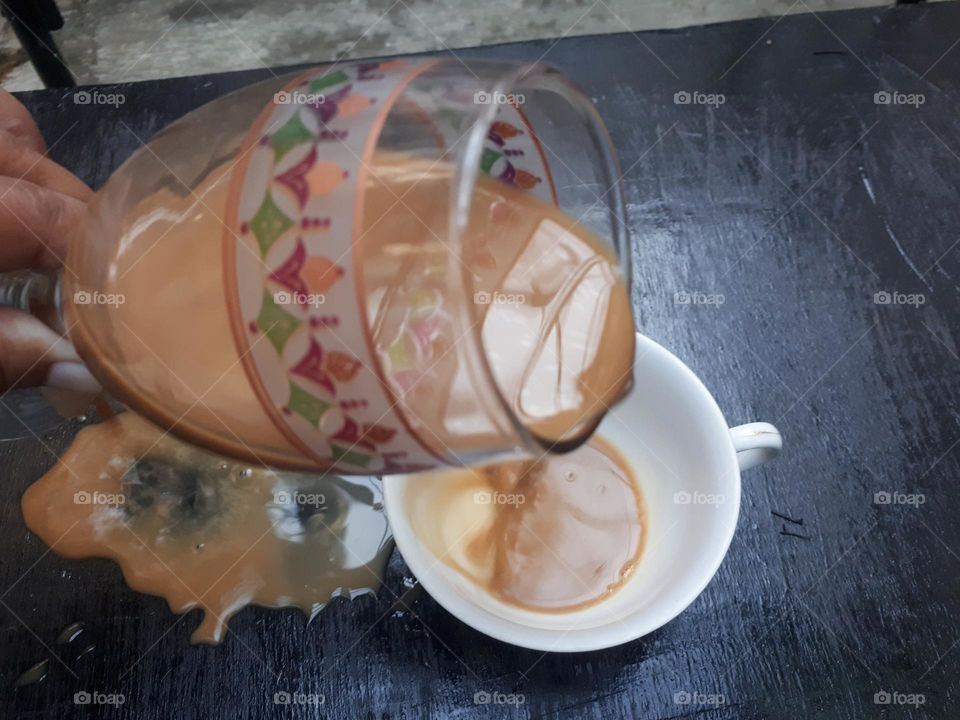 a cup of mocha coffee that was being poured but spilled over a small glass in the morning