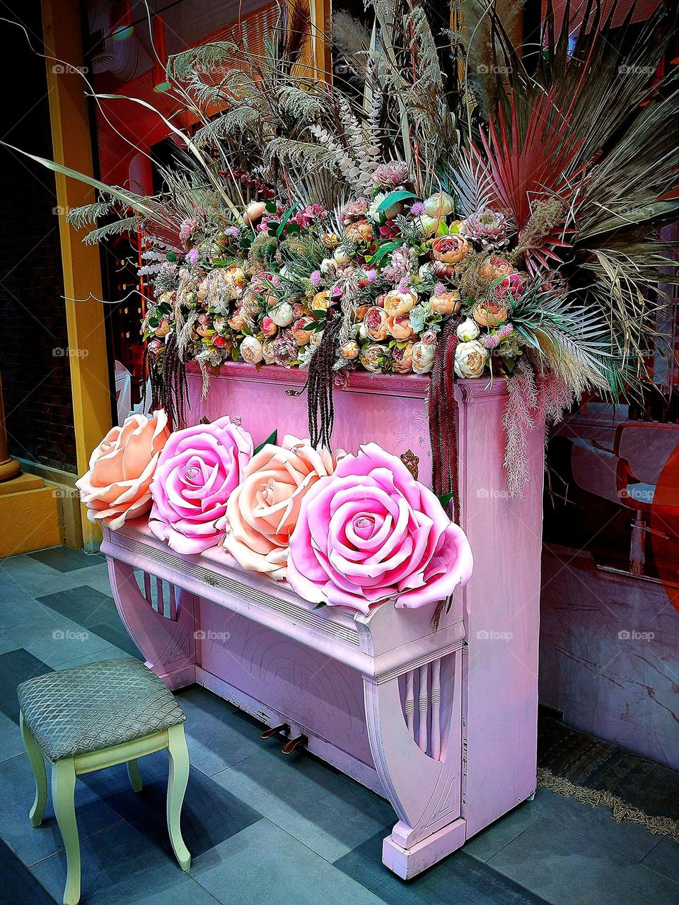 Baby pink. A baby pink piano with artificial roses in different shades of pink on the lid. On the top of the piano lie multi-colored flowers and ears of cereals.