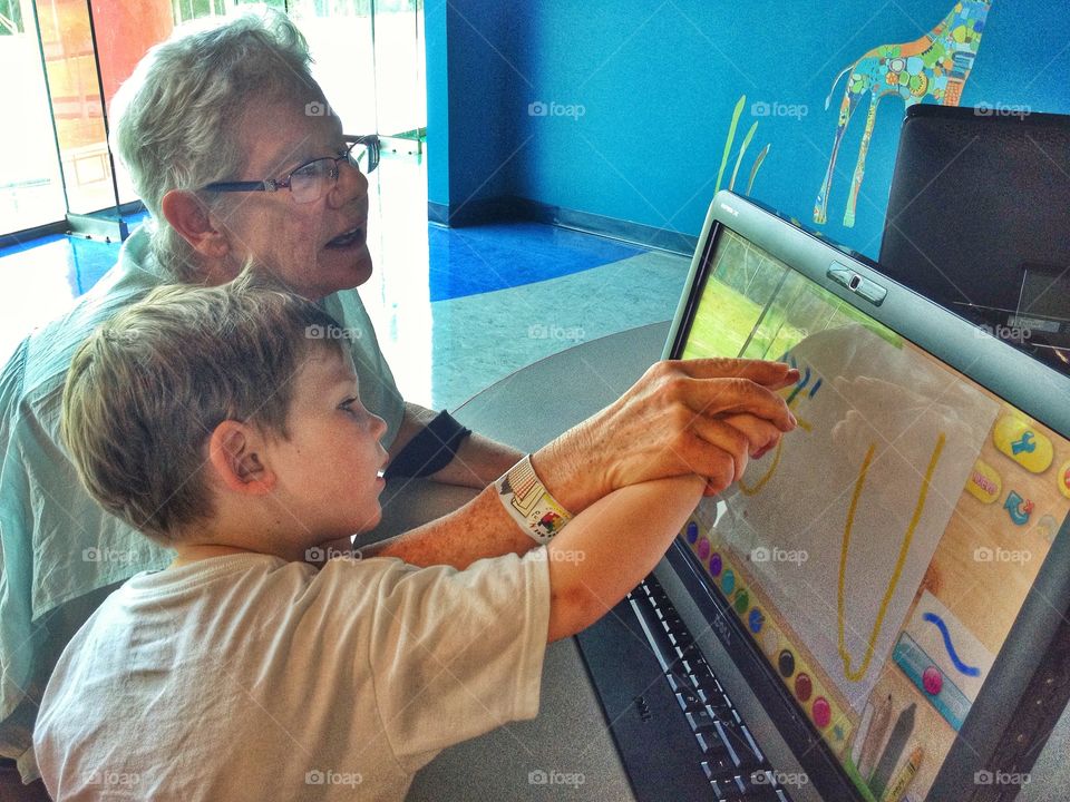 Desk From Above. Child Teaching Grandma How To Use A Computer
