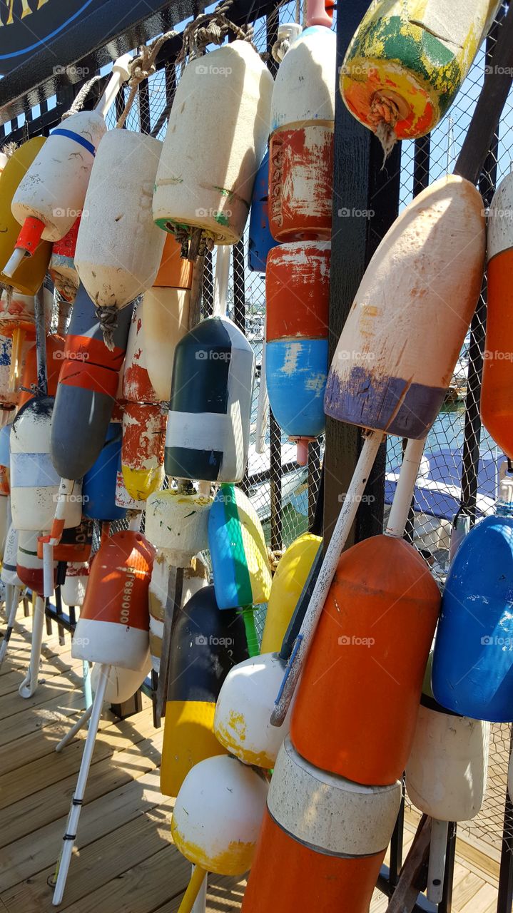 A colorful collection of maritime bobbins and buoys hang on a pier fence in the city.