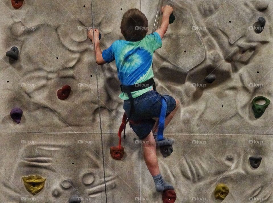 Young Boy Bouldering. Little Boy Tackling A Rock Climbing Wall
