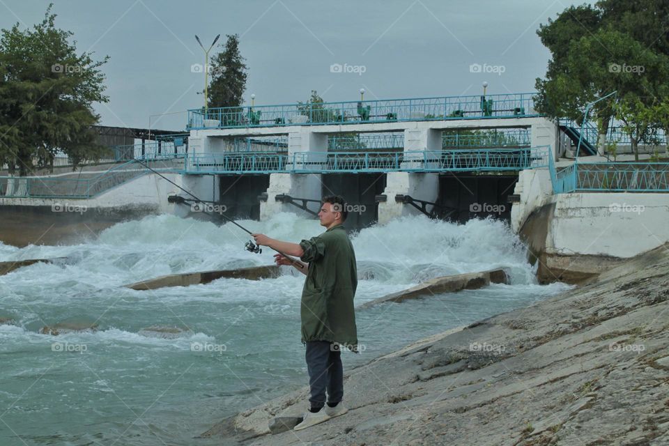 young fisherman catches fish on a spinning rod near the dam