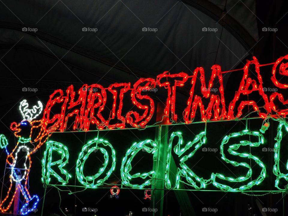 A reindeer with “Christmas Rocks” sign made out of red and green Christmas lights lit up after dark. 