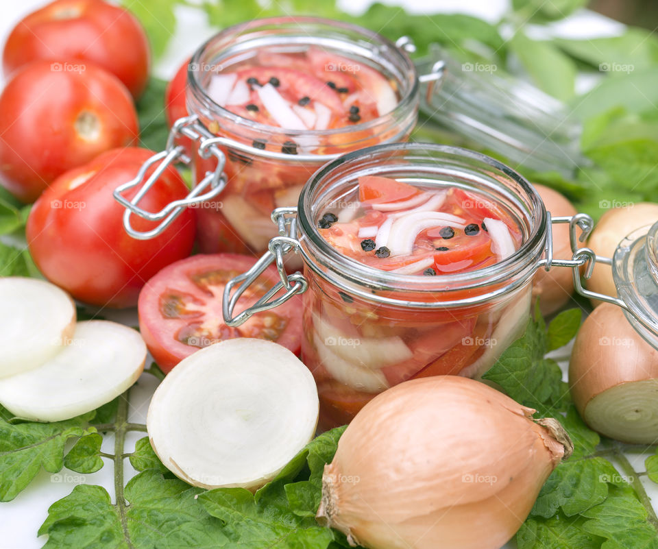 Two open glass storage  jars full of pickled tomatoes, onions chopped into small pieces and black peppercorns.