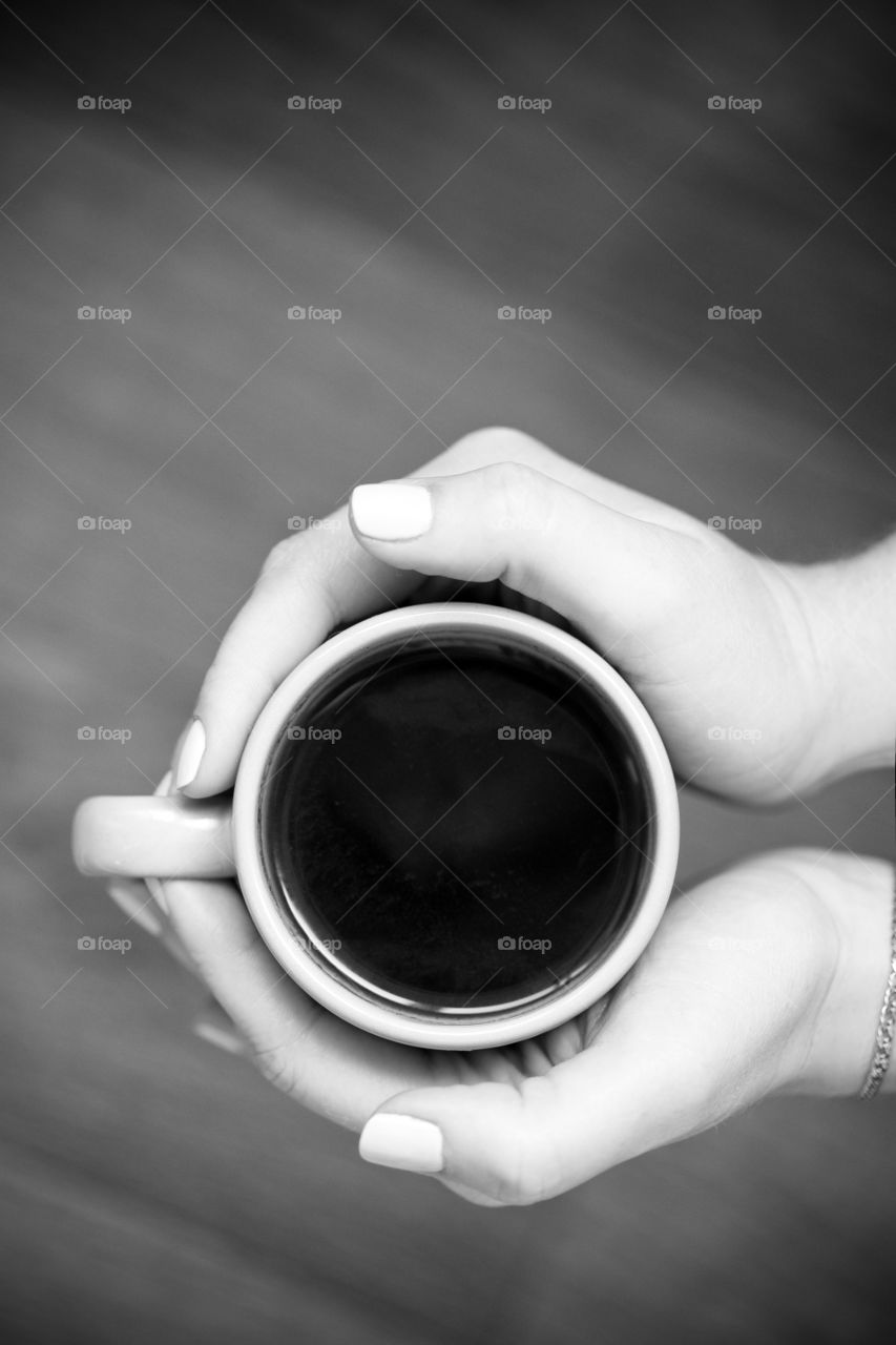 Cup of coffee in hands, top view, vertical shot in black and white