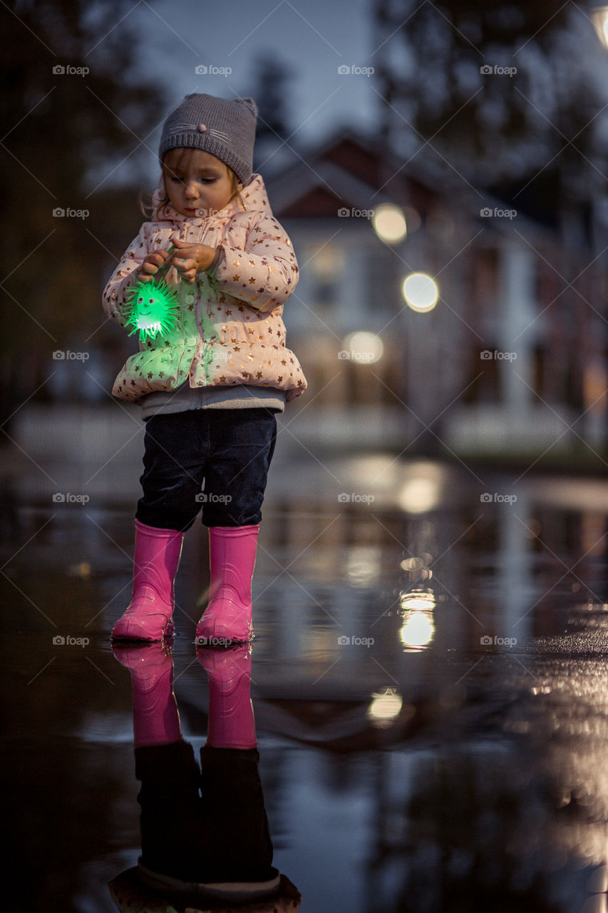 Little girl  in waterproof boots playing in a puddle 