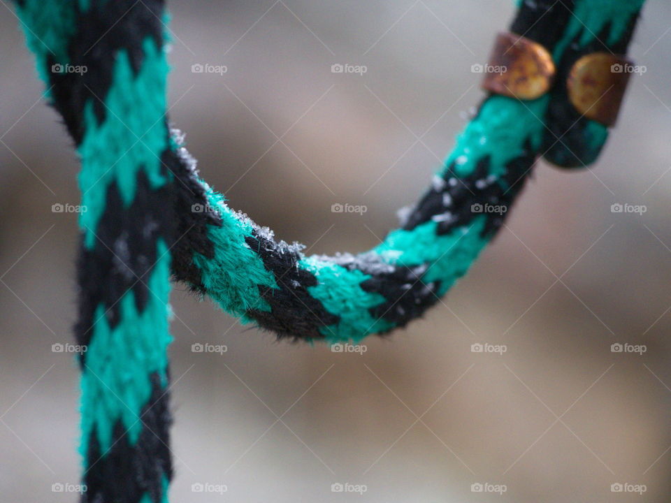 A turquoise and black striped lead rope hanging outside with a rusty clasp and a light dusting of snow