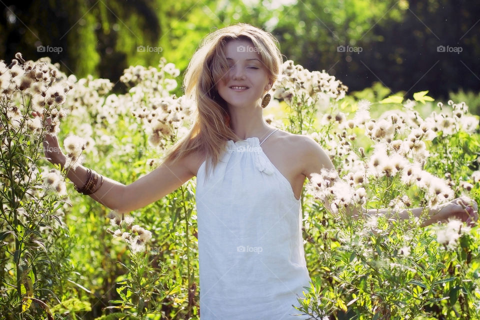 Young attractive girl in linen dress enjoy nature field with white fluffy flowers 