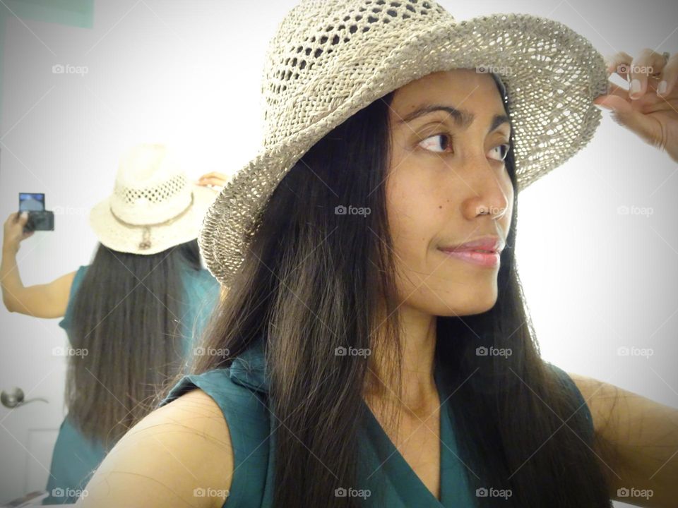 A woman with long hair wearing a hat doing selfie.