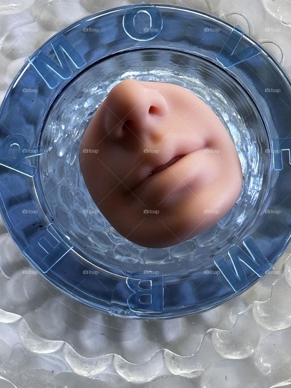 Caucasian silicone nose model in blue glass dish with MOVEMBER letters on rim on clear bubble pattern glass plate