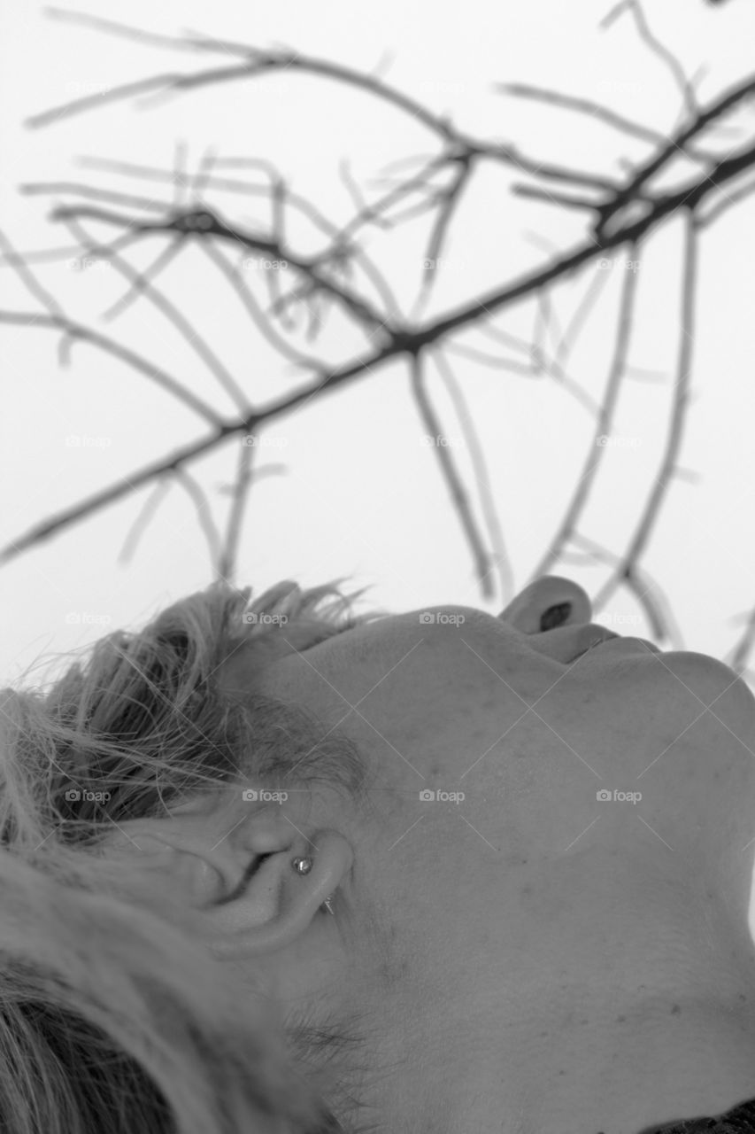 The model looks up. Above are dry branches of trees. The photograph is made in black and white. Only part of the face is visible to the model.