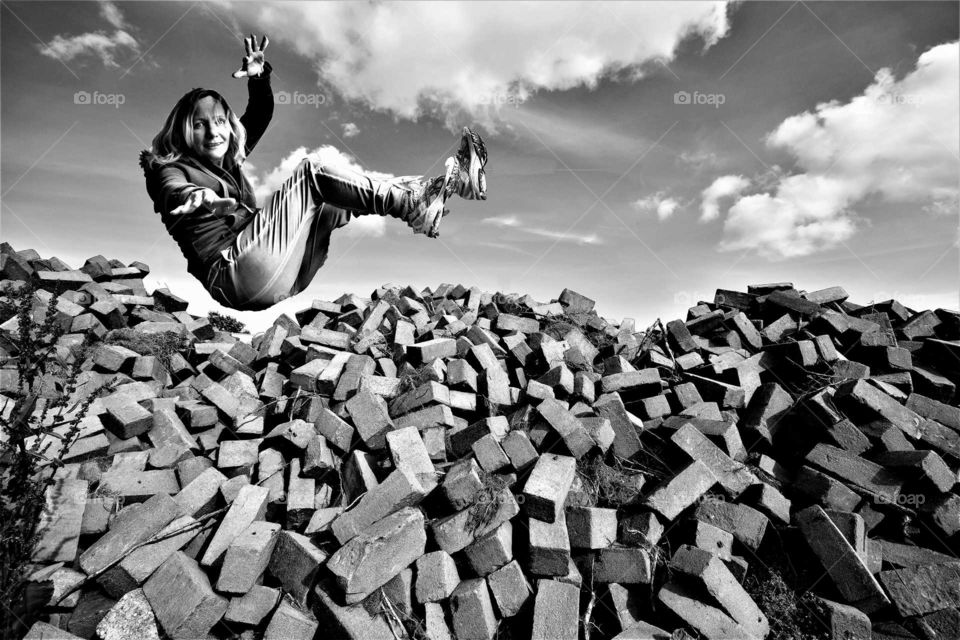 black and white forced perspective picture woman flying above piles of stone bricks