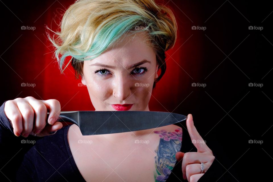 Attractive young Caucasian woman with partly visible tattoo holds a silver knife with her finger on the point. 