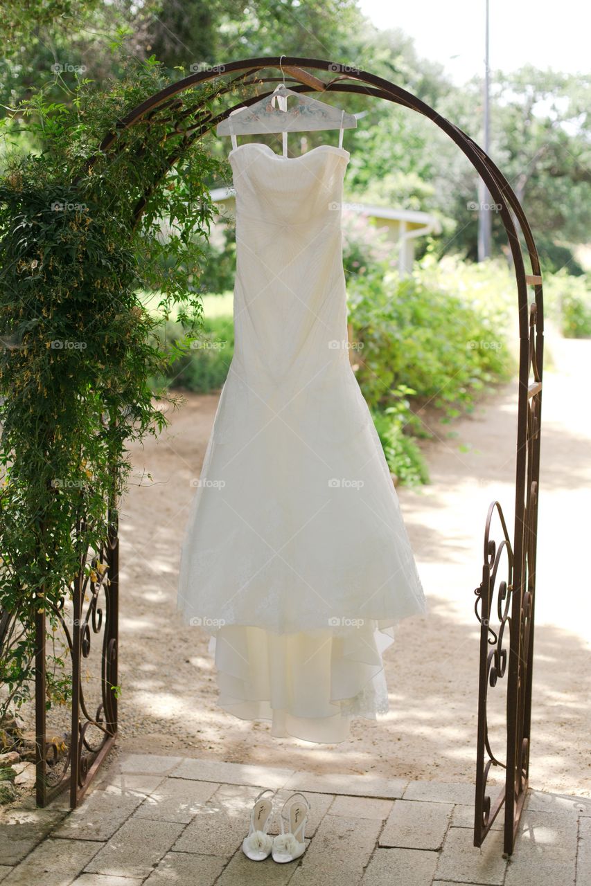 Brides wedding dress hanging outside with her shoes in an archway
