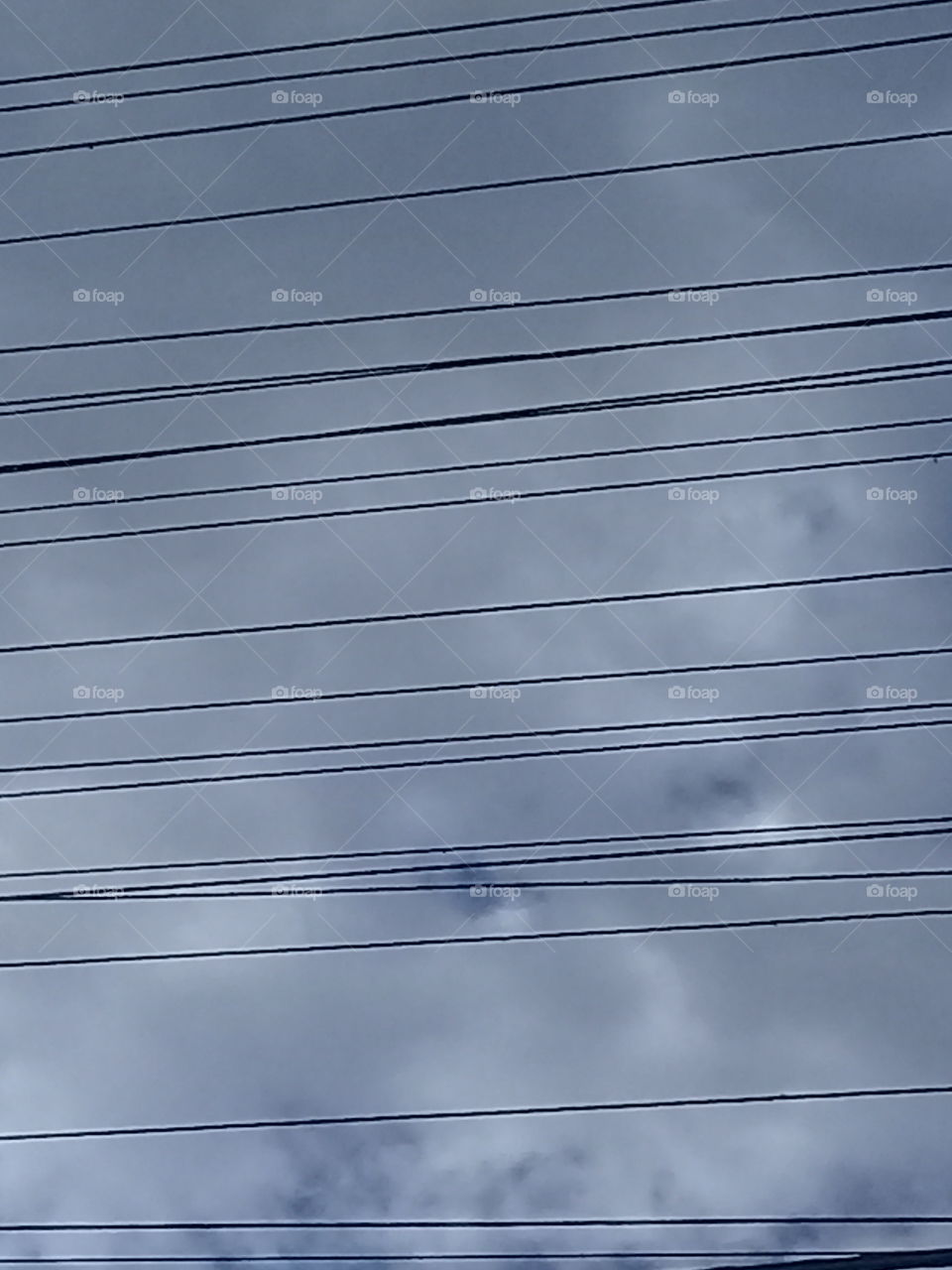 imagen de cables eléctricos de alta tensión cubriendo de rayas un cielo nublado de verano.