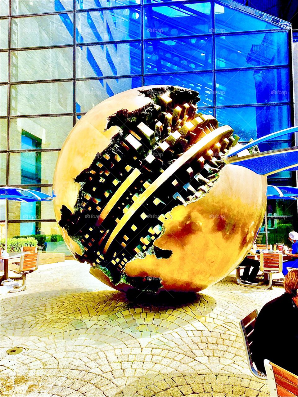 A gigantic golden ball at Mt Sinai hospital in Manhattan. The golden sphere’s surface looks shattered as if it was a broken Christmas ornament and reveals inside it what looks like the gears of a precision watch. 2020. Hypnotic Productions