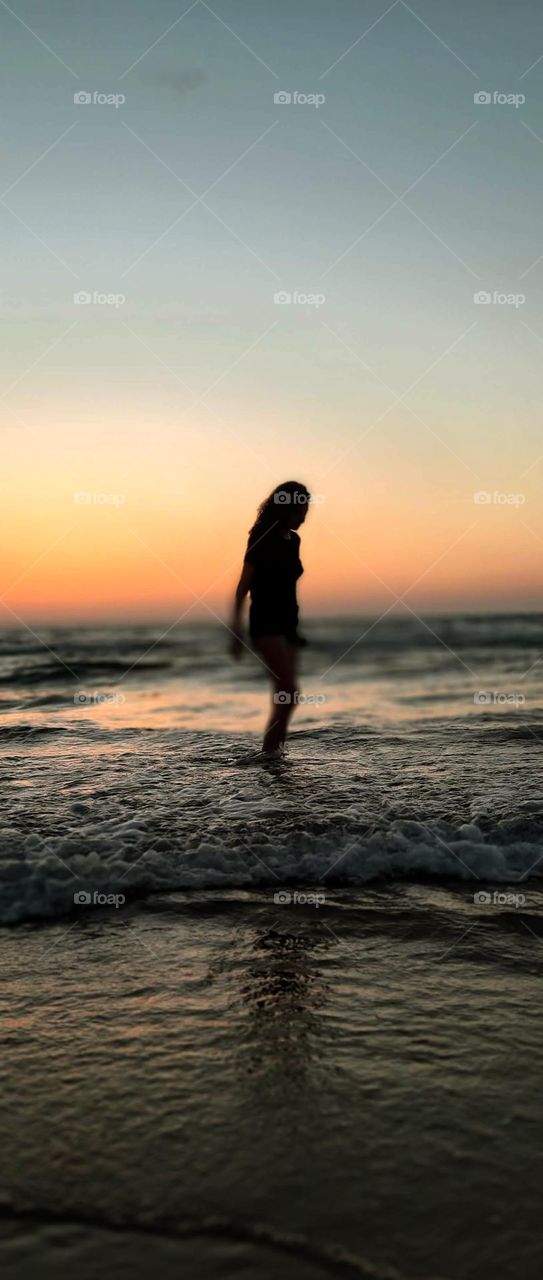 a beautiful young woman walking on the beach in tel aviv during sunset