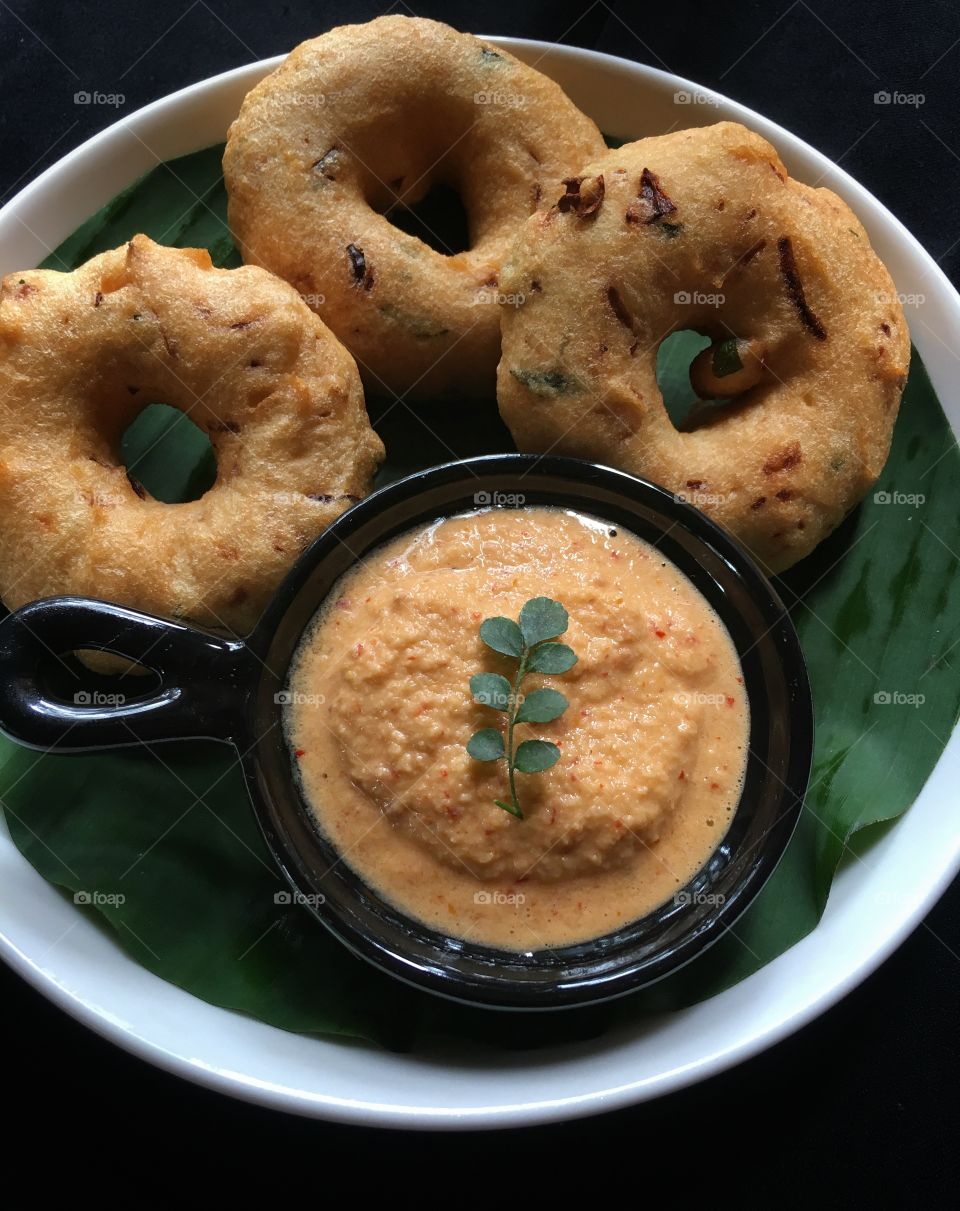 Delicious Medhu vadai with chilli chutney served in a white ceramic plate with a banana leaf .