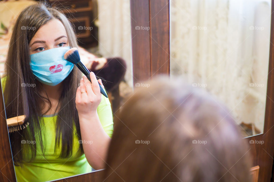 A young girl does makeup for a walk outside in a protective mask against the coronavirus pandemic, her lips are painted with red lipstick.