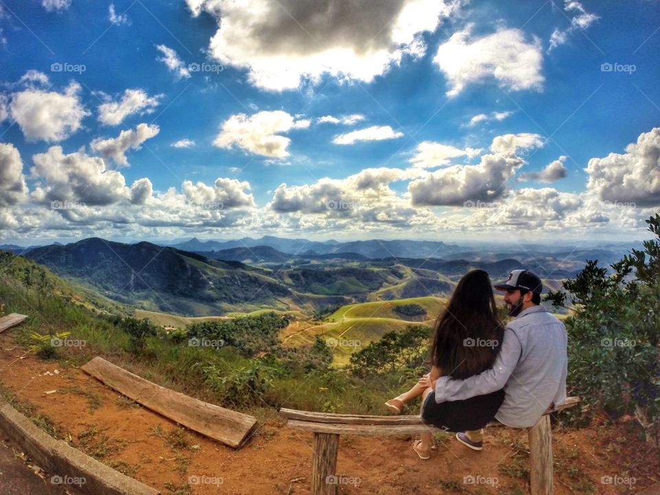 Rear view of couple sitting on bench against scenic landscape