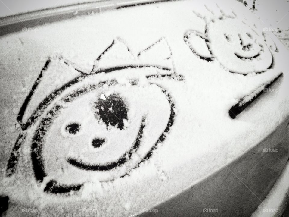 Finger drawings of children faces on the car glass covered with snow. Black and white.
