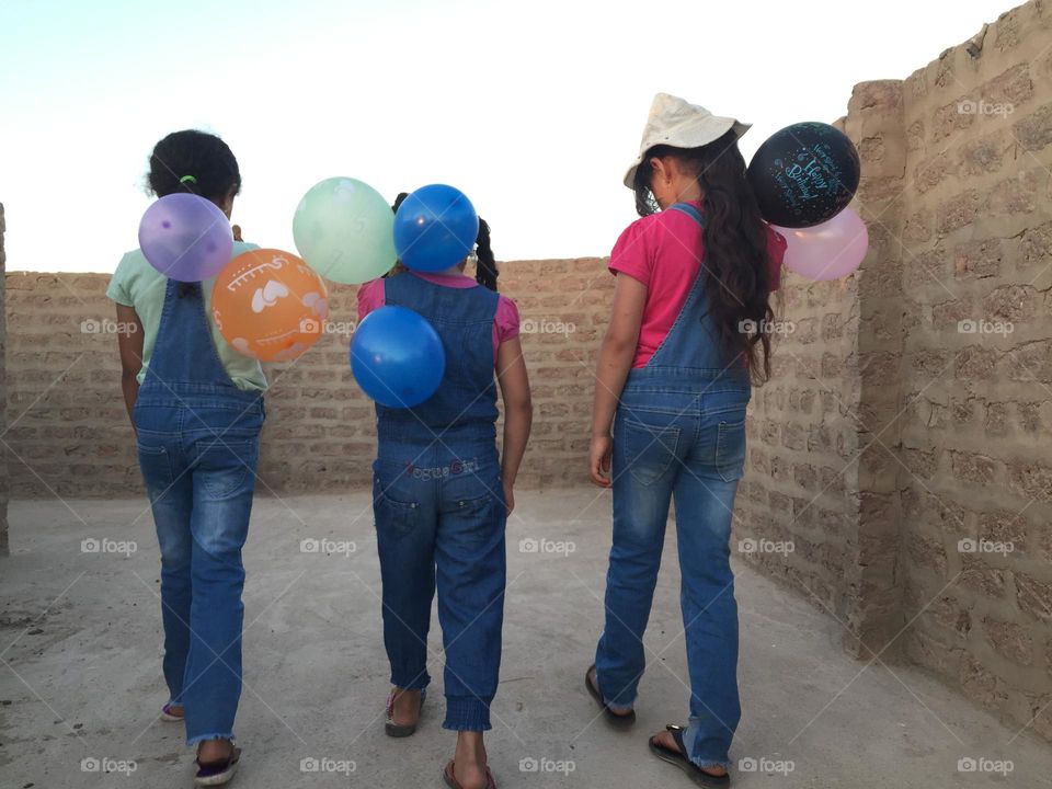 Three little girls are walking and holding some balloons 