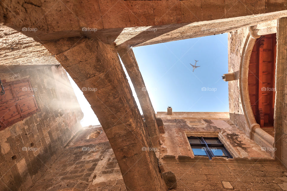 Old medieval masonry building in Rhodes downtown with framed view of flying above aeroplane.
