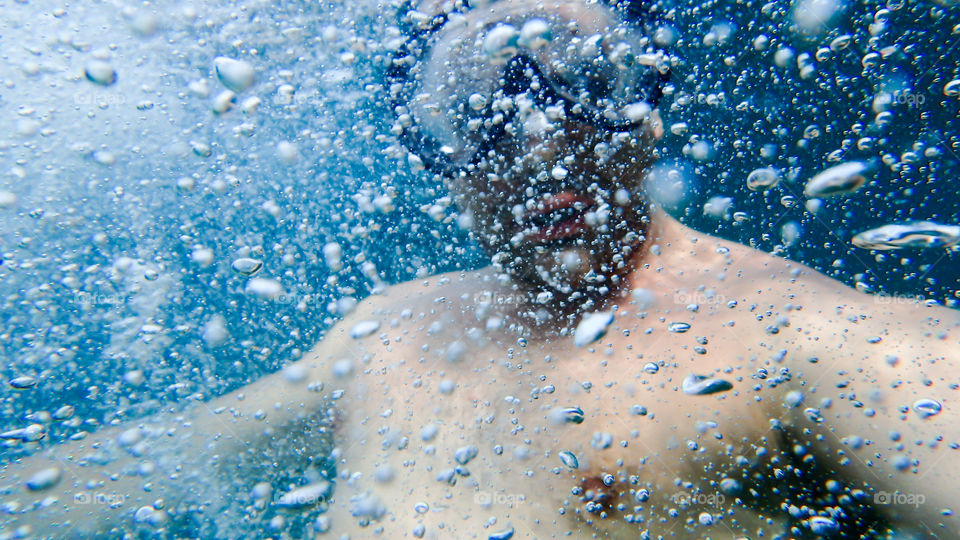 Man diving, male underwater smiling,swimming and relaxing in big blue sea with his camera