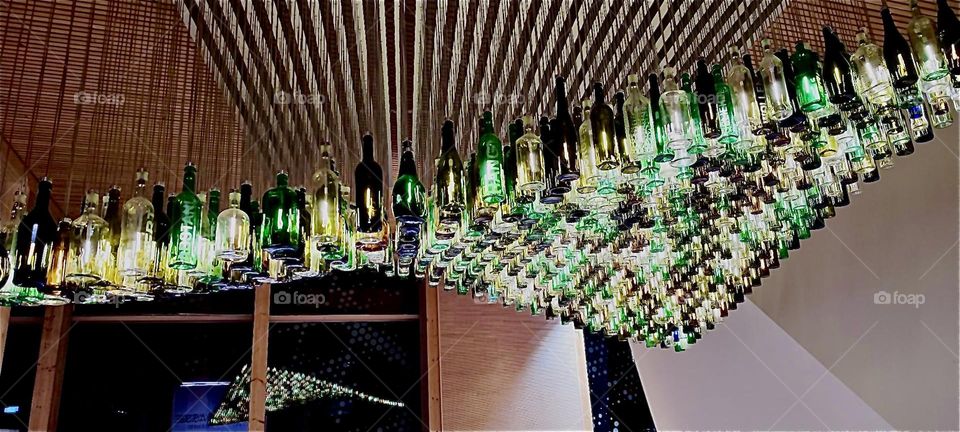 This is an installation of individually suspended bottle lamps fitted with a fixture that gets switched on and off on a dimmer for an impressive light show. The place is the „Navareum“ in „Straubing“, Germany. 2023. Hypnotic Productions