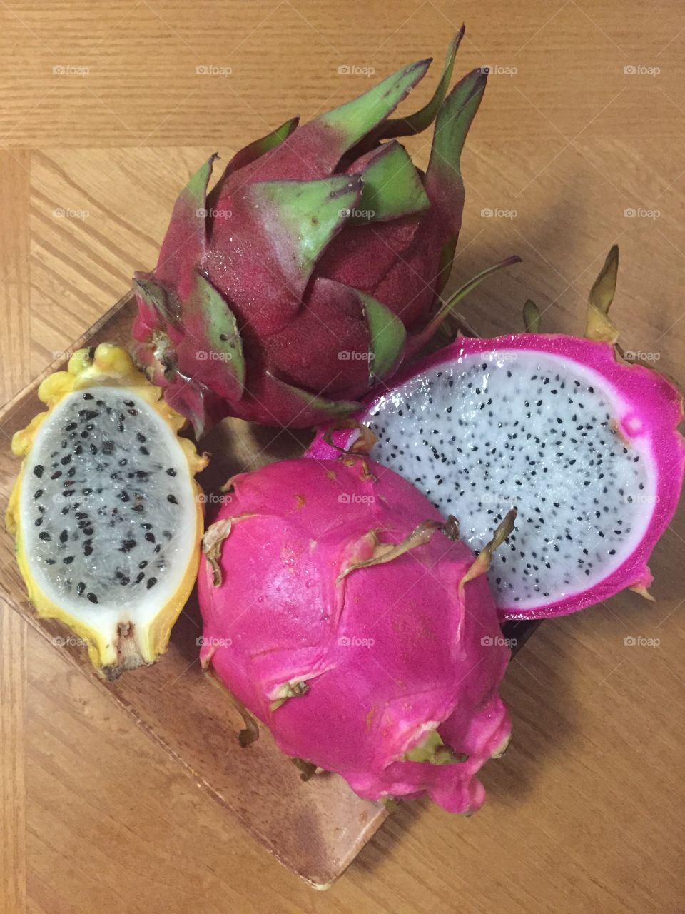 Pink, red and yellow dragon fruits in a wooden plate on wooden table 