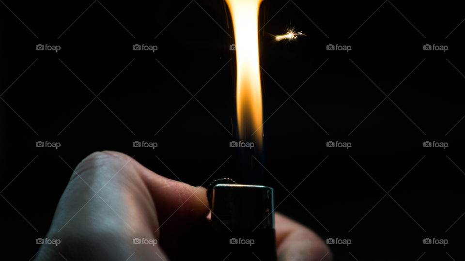 A person has lighters in his hands and he lights it through a flint wheel, the lighter ignites, sparks and fire appear, close-up on a black background.