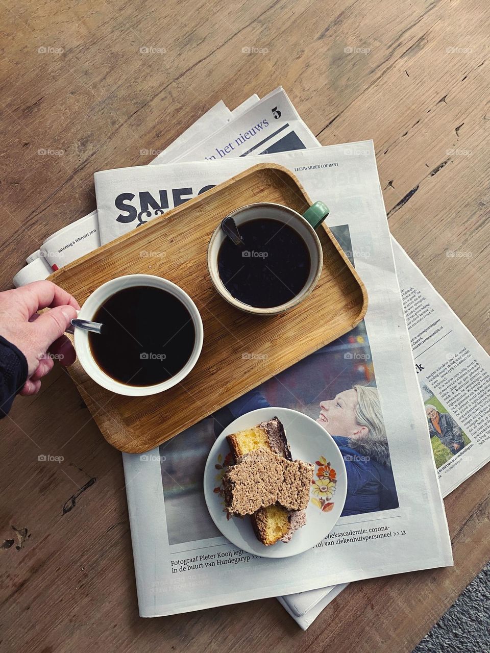 Coffee photography, coffee cups with coffee on a tray. Papers and coffee with cake on the wooden table, hand stirring the coffee