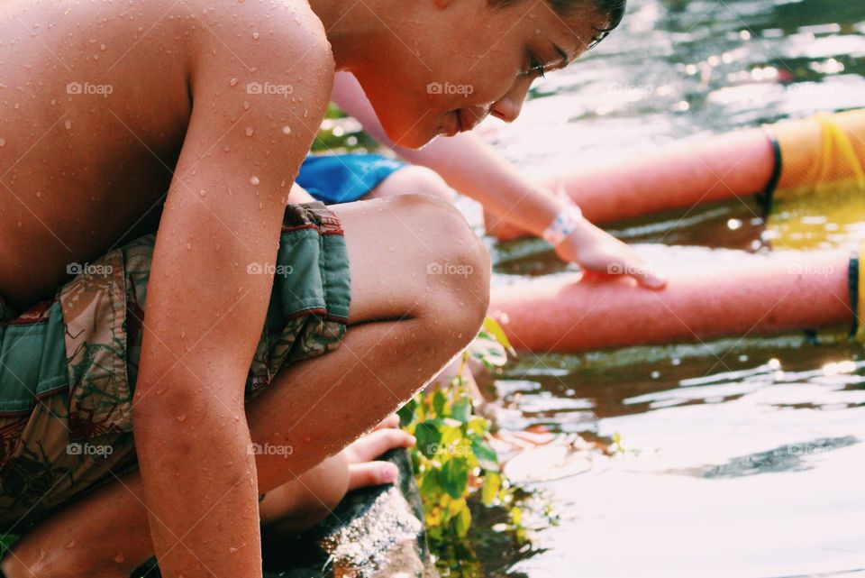 Close-up of shirtless boy crouching near river side