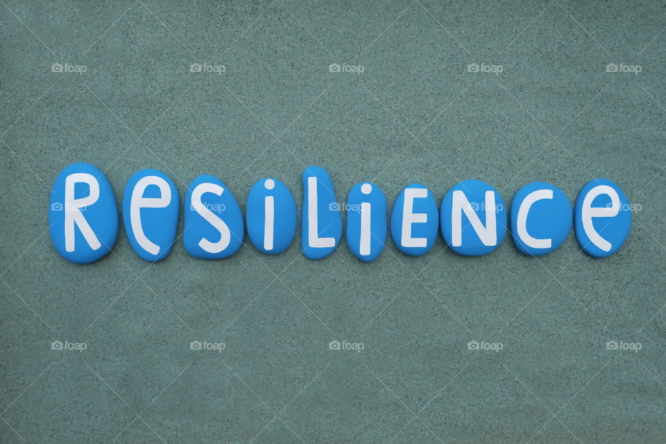 Resilience word composed with blue handmade painted stone letters over green sand