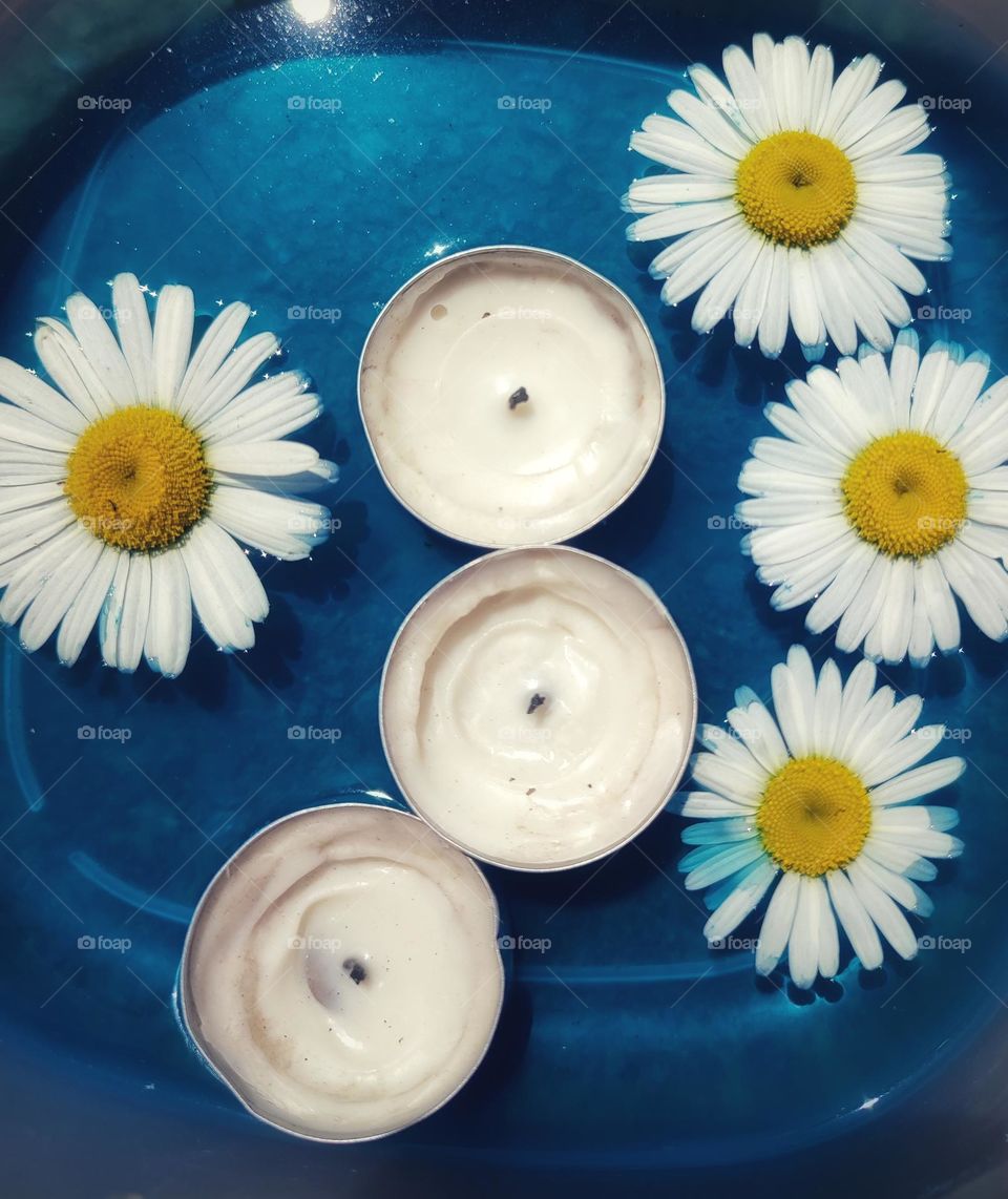 Daisy flowers and candles floating on blue water