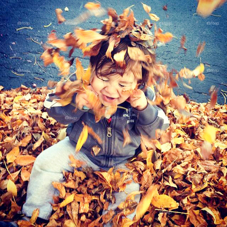 Falling leaves on toddler. Silly toddler plays in a pile of leaves
