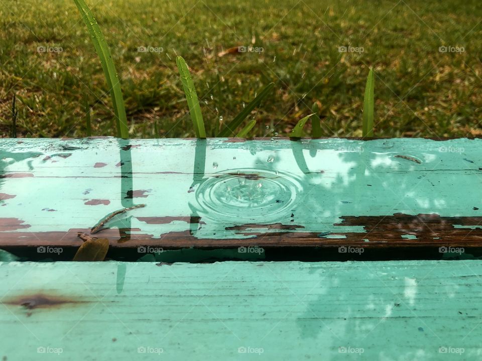 Raindrop splashing on closeup of turquoise painted porch step into grassy backyard 