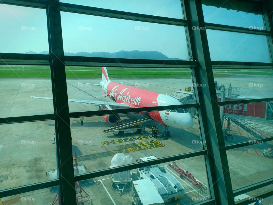 Aircraft of Air Asia parks at airport, view from waiting room in airport Penang Malaysia.