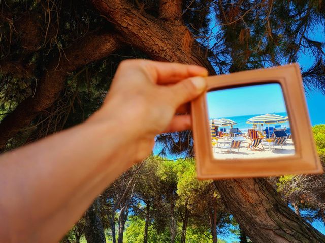 hand holds a mirror that reflects the beach and the umbrellas by the sea