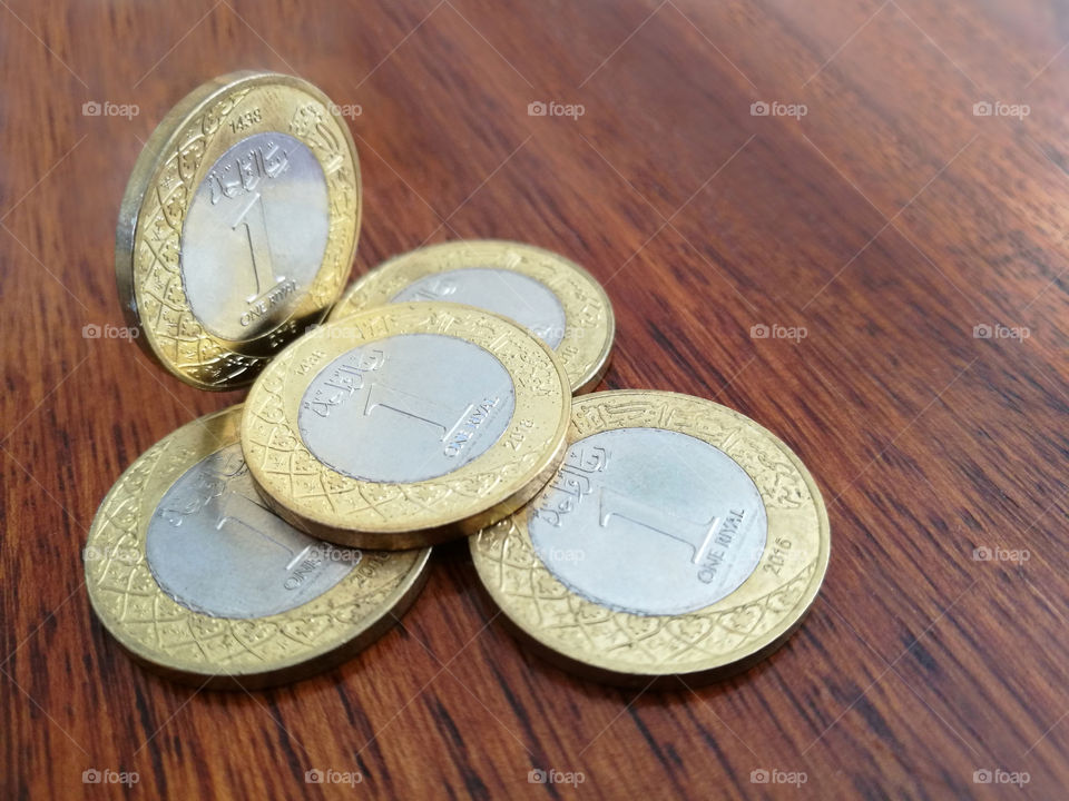 Saudi Arabia 1 Riyal coins, 1438 (2016) on wood table with blurred background.
