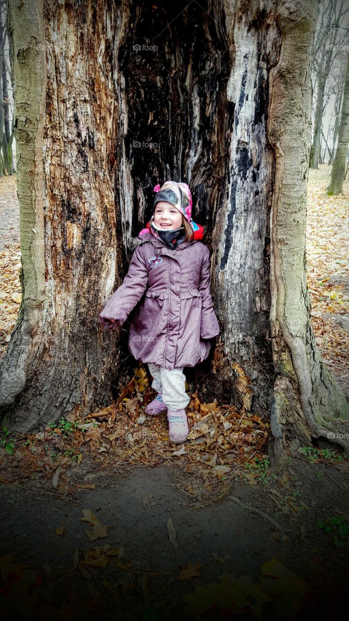 Small girl standing near tree trunk