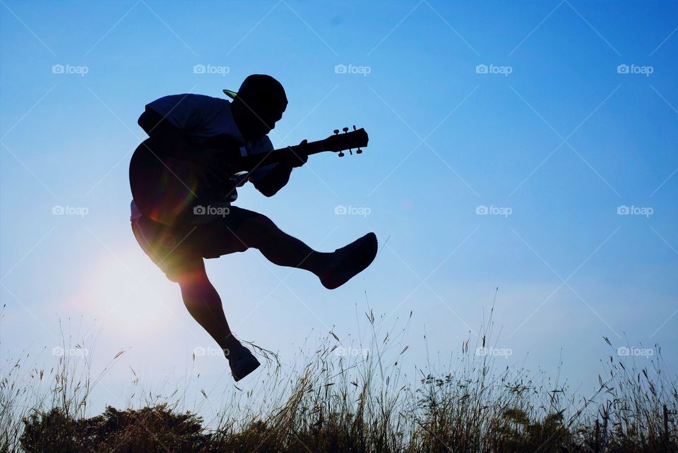 A man jumping play guitar on sky background.