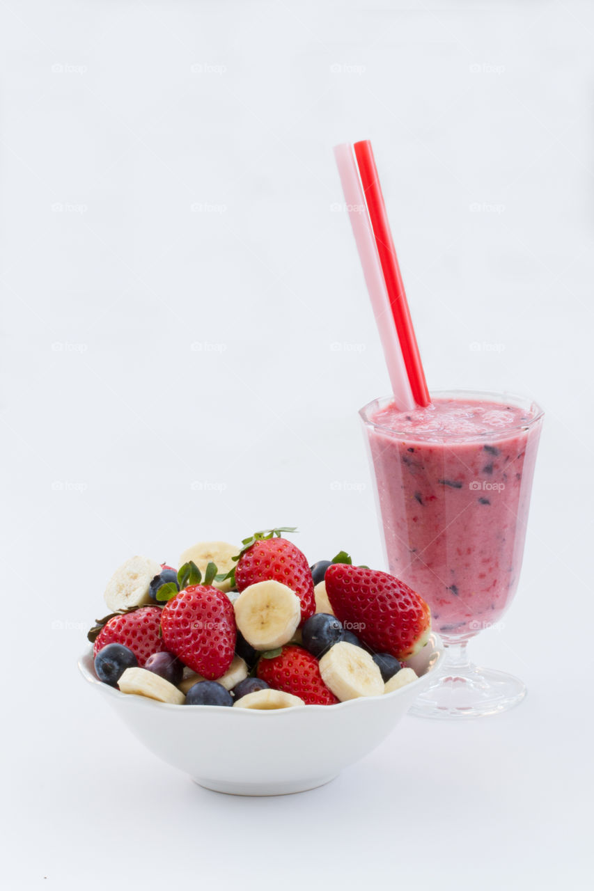 A smoothie and ingredients made from strawberries, blueberries and bananas on an isolated white background.